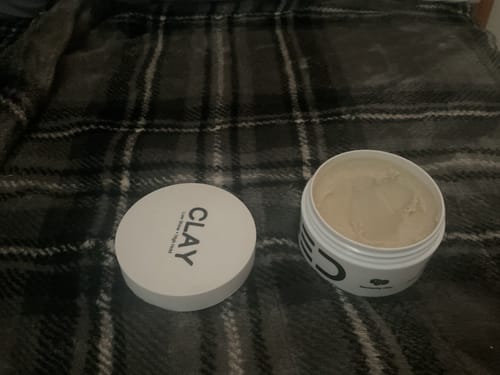 Reviewer's open jar of Hair Clay with the lid placed next to it on a plaid surface.
