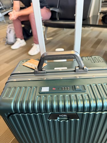 Close-up of a reviewer's green All-in-One Carry-On, showing the top handle and TSA-approved lock in an airport.
