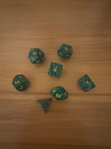 Reviewer's green Malachite Stone Dice Set with gold numbers on a wood surface.