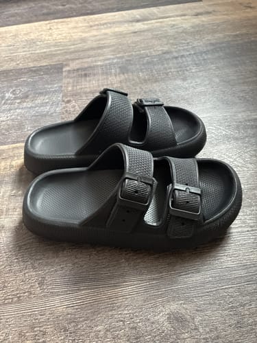 Customer's pair of black Cloudies™ sandals with thick soles and double adjustable straps on a wood floor.