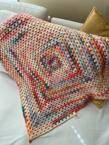 Customer's crocheted pillow from the Hearthside Rainbow Kit, showing the colorful granny square pattern resting on a sofa.