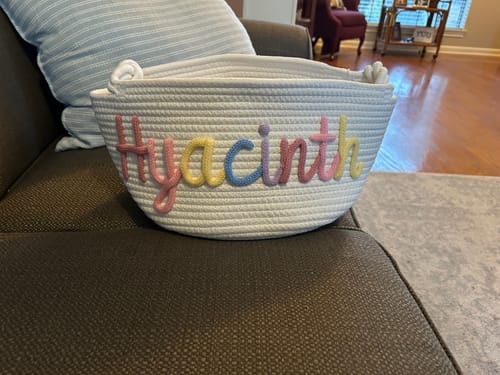 Customer's white personalized knitted basket with the name 'Hyacinth' in multicolor yarn, sitting on a couch.