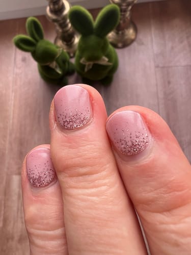 Nahaufnahme der Hand eines Kunden mit den 'Cupcake Sprinkles' UV-Gel-Nagelfolien in einem Ombré-Glitzerdesign in Rosa.