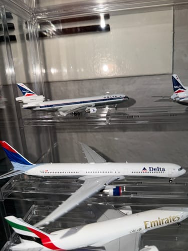 Close-up of a reviewer's HERPA DELTA MD-11 model airplane on a shelf inside a clear display case with other models.