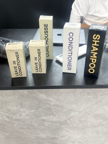 Customer's box for Curl Mousse shown with other hair products from the same line on a desk.