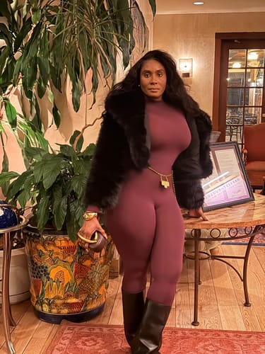 Reviewer wearing the form-fitting maroon Naked Closed Toe Jumpsuit, styled with a black fur jacket and boots.