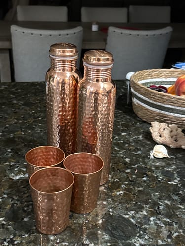 Reviewer's set of two hand-hammered Pure Copper Water Bottles and four matching cups on a kitchen counter.