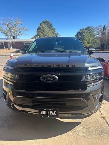 Customer's New Mexico Blackout Metal License Plate with 'WOLFPAC' text, mounted on a dark gray SUV.