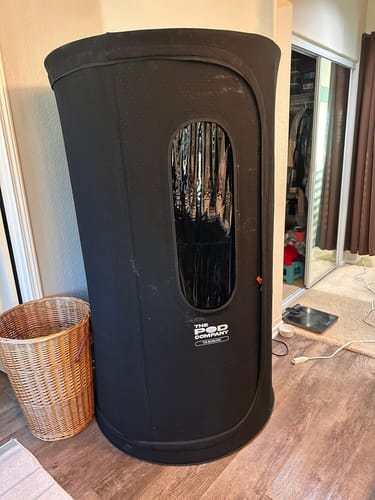 Reviewer's black Sauna Pod 2.0 set up in a bedroom, showing its compact size.