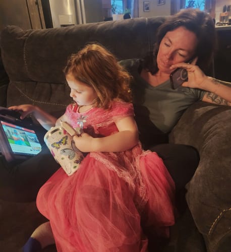 Customer's child holding the Butterfly Spill Proof Kids CREWCUP while sitting on a couch next to a tablet.