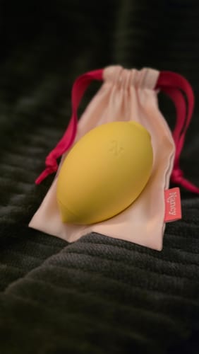 Customer's yellow Lem Clitoral Massager resting on its soft pink storage pouch on a dark blanket.