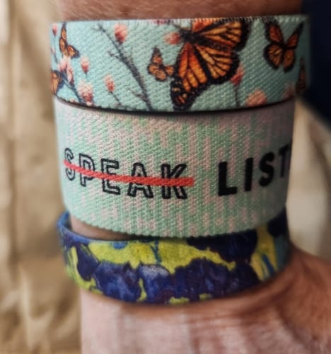 Close-up of a reviewer's wrist wearing three straps from a Mystery 3-Pack, featuring butterfly, text, and floral designs.