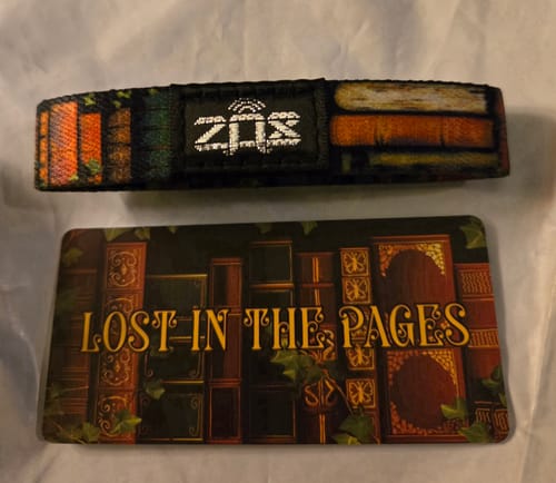 Customer's Lost In The Pages Bracelet showing a bookshelf design, laid flat next to its matching card.