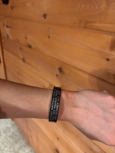 A person wearing a customized black memorial bracelet on their wrist, showing the personalized three-line inscription.