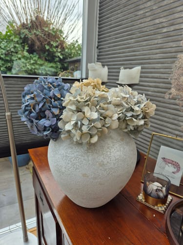 Klant toont de witte Sena vaas op een houten dressoir, gevuld met grote, gedroogde bloemen.