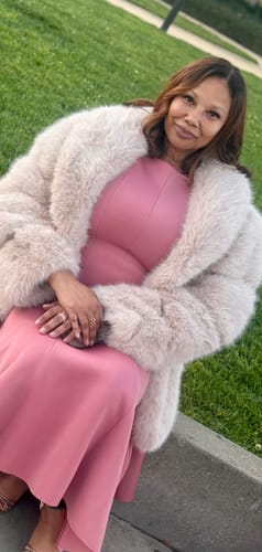 Reviewer sitting outdoors wearing the plush Faux Mink Pelted Coat open over a pink dress.