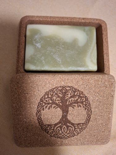 Kunde zeigt ein Gratis-Sample: eine grün-weiß marmorierte Seife in einer Reisebox aus Kork mit einem Baum-Symbol.