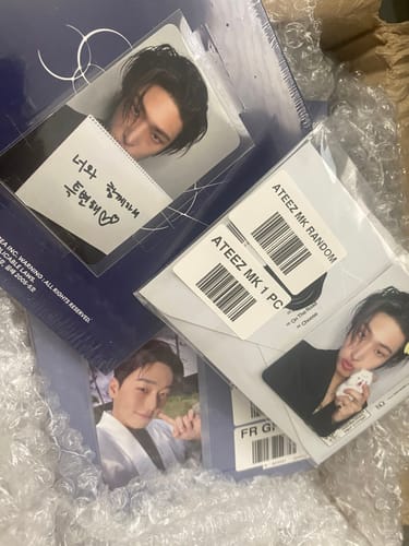 Close-up of a reviewer's ATEEZ GOLDEN HOUR album and member photocards partially unboxed from shipping packaging.