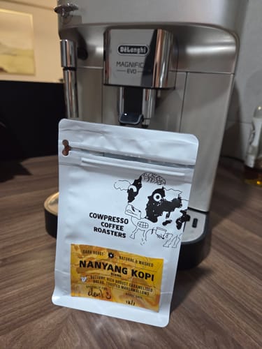 Customer's Nanyang Kopi Roast in its white pouch, placed in front of a silver coffee machine on a counter.