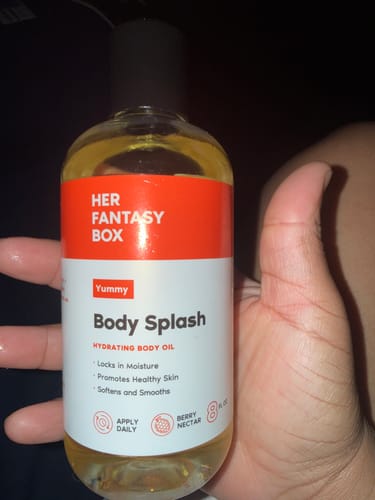 Reviewer's hand holding the clear bottle of Yummy Body Splash hydrating body oil.