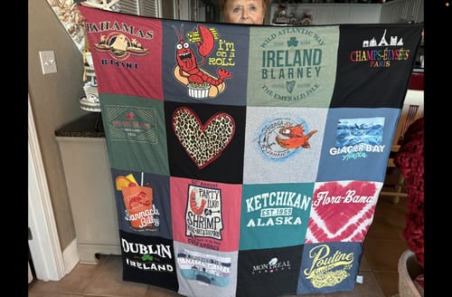 Customer holding up their finished Project Repat T-Shirt Quilt made from colorful t-shirts from travel destinations.