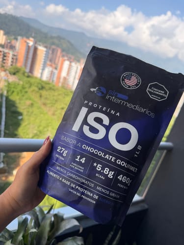 Cliente sosteniendo la bolsa de Proteína Aislada ISO sabor Chocolate en un balcón con una ciudad de fondo.