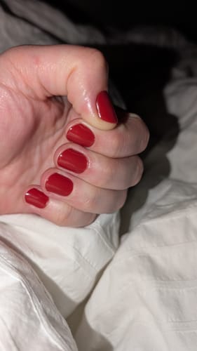 Nahaufnahme der Hand einer Kundin mit den glänzenden roten 'Burning Lava' UV-Gel-Folien auf kurzen Nägeln.