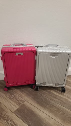 Customer's two Check-In: All-In-One 28" suitcases, one pink and one silver, standing on a wood floor.