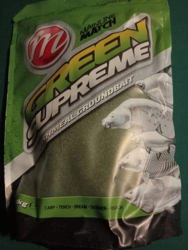 Recensent toont de groene, afgesloten zak Green Supreme Fishmeal grondvoer.