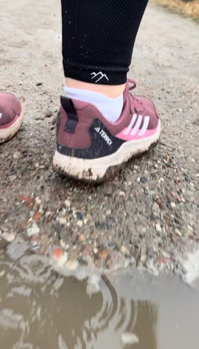 Nahaufnahme der Tofana Leggings eines Kunden, die bei einer Wanderung auf einem schlammigen Weg getragen wird.