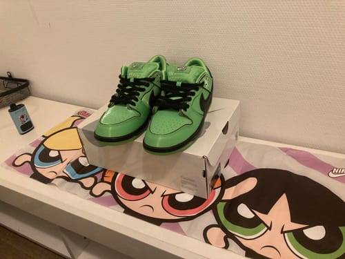 Klant toont de groene Nike SB Dunk Low The Powerpuff Girls Buttercup sneakers op de schoenendoos bovenop een Powerpuff Girls-mat.