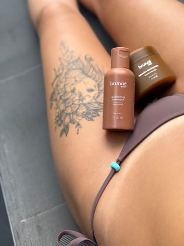 Customer's bottle of Accelerating Tanning Oil resting on their tanned leg while sunbathing.