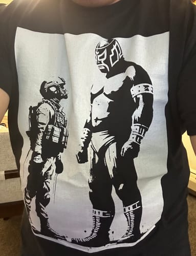 Customer wearing the Sin Lucha No Hay Victoria T-Shirt, showing a graphic of a luchador facing off with a soldier.