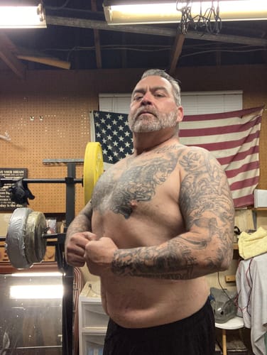 Customer showing his physique progress by flexing his bicep and chest in a home gym.