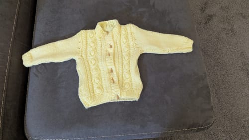 Reviewer's finished Sirdar 4783 Cardigan in pale yellow aran yarn, laid flat on a dark grey sofa.