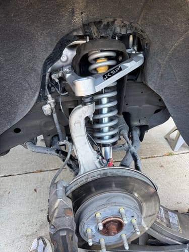 Customer's silver KSP Forged Aluminum Upper Control Arm installed on a truck's front suspension, with the wheel removed.