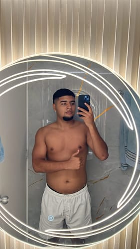 Cliente mostrando su físico frente a un espejo, ilustrando los resultados del uso de la Creatina Monohidrato.