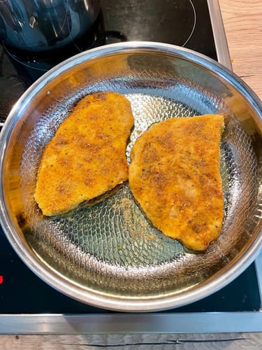 Rezensent brät zwei goldgelbe Schnitzel in der fein gehämmerten Titanpfanne auf einem Kochfeld.