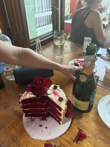 A customer's sliced Regal Rose Velvet Cake, topped with a red rose, on a celebration table.