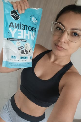 Una clienta en ropa deportiva sostiene el empaque de Proteína Whey - Cookies & Cream.