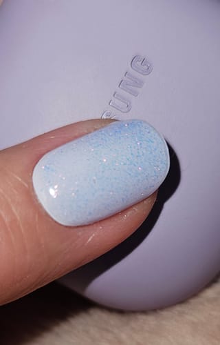 Kundin zeigt in Nahaufnahme das schimmernde Finish des UV Top Coat Pink Pearl auf ihrem Nagel.