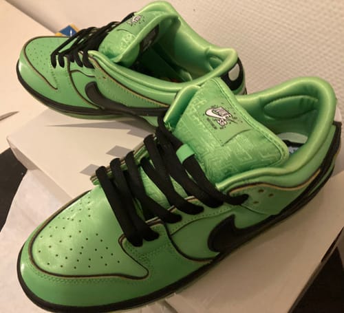 Close-up van de zijkant van de glanzende groene Nike SB Dunk Low Buttercup sneakers van de klant.