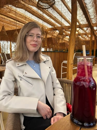 Kundin trägt die zarte Glow Clover Kette mit einem blauen Oberteil in einem Café.