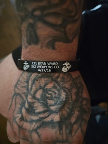 Customer wearing their customized black bracelet with text and Marine Corps emblems on a tattooed arm.