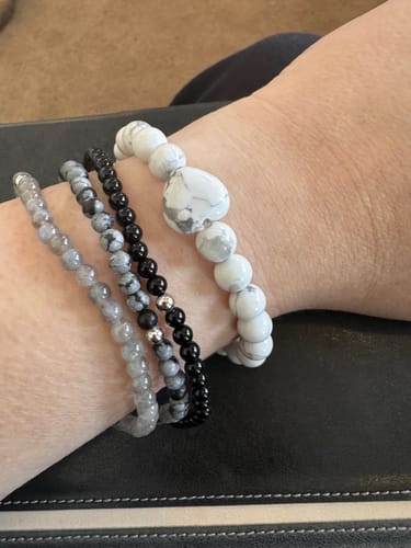 Reviewer's wrist wearing the white howlite bracelet with a heart-shaped stone, stacked with three smaller bracelets.