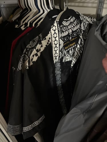 Reviewer's black Azteca Guayabera with detailed patterns on the collar and shoulders, hanging in a closet.