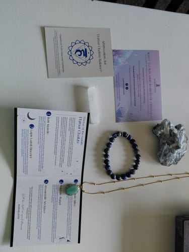 Customer's AuraBloom Subscription Box contents laid out, showing a crystal bracelet, necklace, various stones, and info cards.