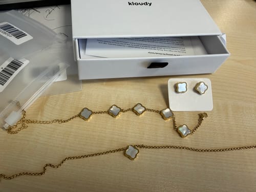 Customer's Valentine Clover Set with a gold-colored necklace, bracelet, and earrings laid out on a wooden desk near its packaging.