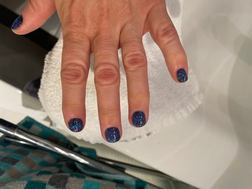 Nahaufnahme der Hand einer Rezensentin mit dunkelblauen, glitzernden „Midnight Thoughts“ UV-Gelnägeln.