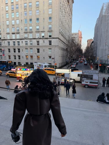 Reviewer from behind wearing the brown Vegan Leather Trench Coat while standing on city steps.